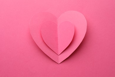 Paper hearts on pink background, top view