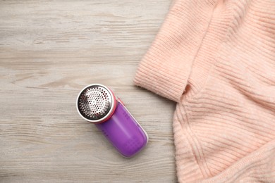 Photo of Modern fabric shaver for lint removing and sweater on wooden table, flat lay