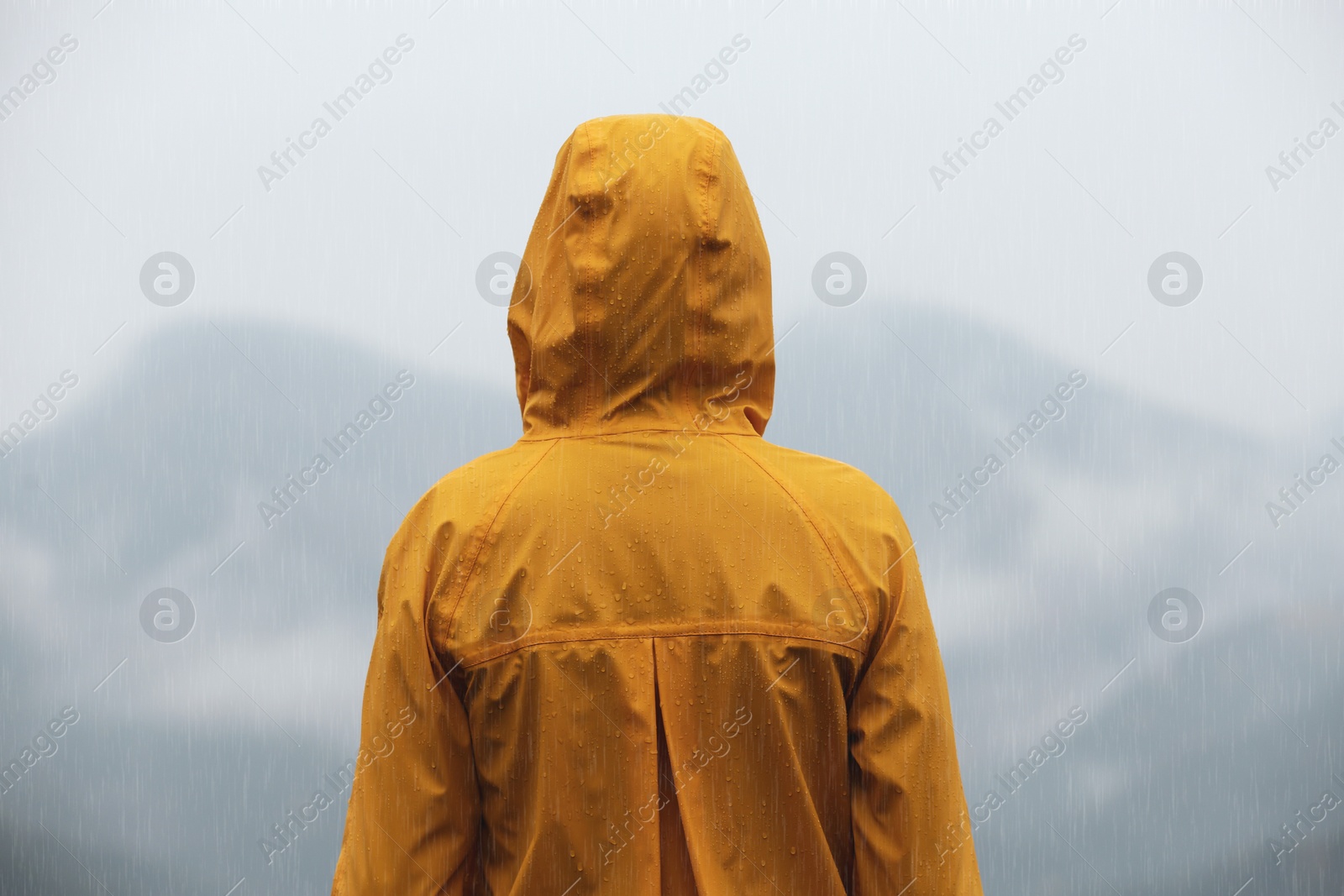 Photo of Woman in raincoat enjoying mountain landscape under rain, back view