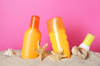 Photo of Different suntan products, seashell and starfishes on sand against pink background