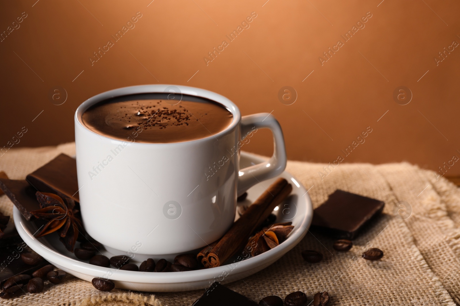 Photo of Cup of delicious hot chocolate, spices and coffee beans on table. Space for text