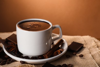 Photo of Cup of delicious hot chocolate, spices and coffee beans on table. Space for text
