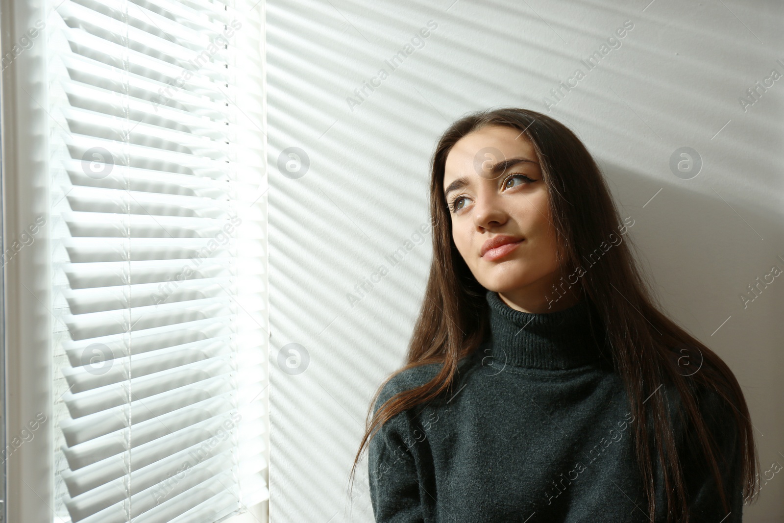 Photo of Young woman near window with Venetian blinds. Space for text