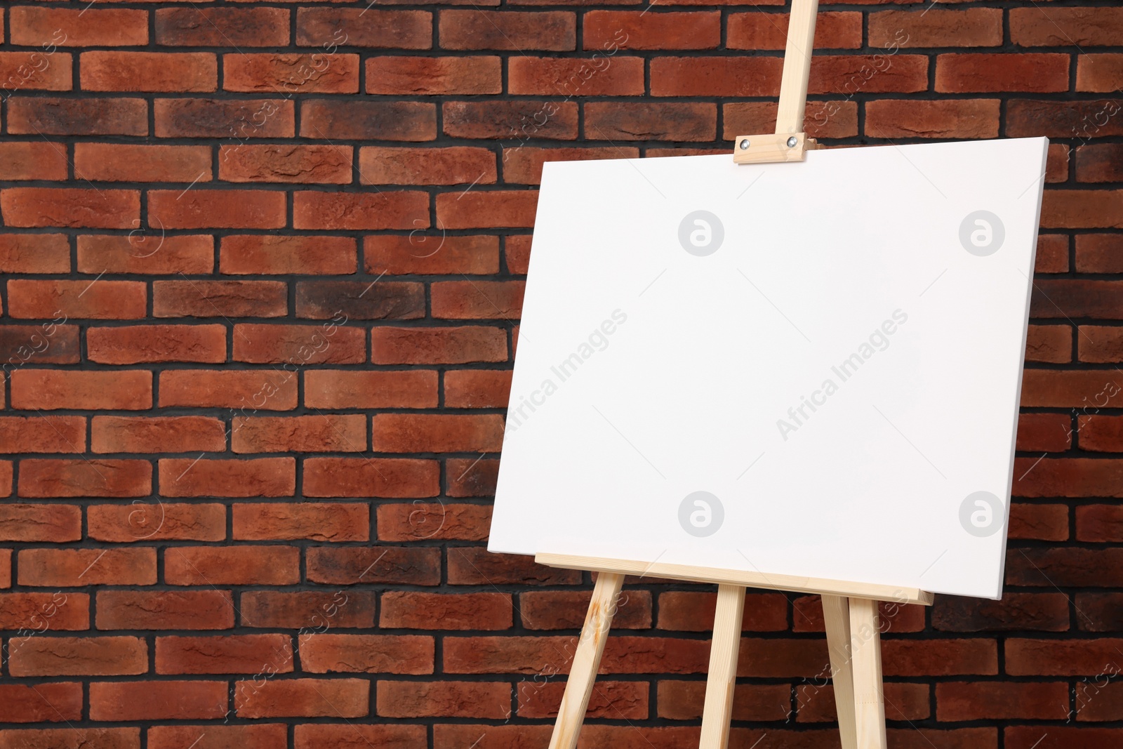 Photo of Wooden easel with blank canvas near brick wall, closeup. Space for text