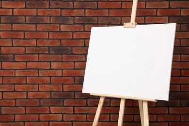 Photo of Wooden easel with blank canvas near brick wall, closeup. Space for text