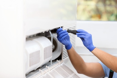 Professional technician maintaining modern air conditioner indoors, closeup. Space for text