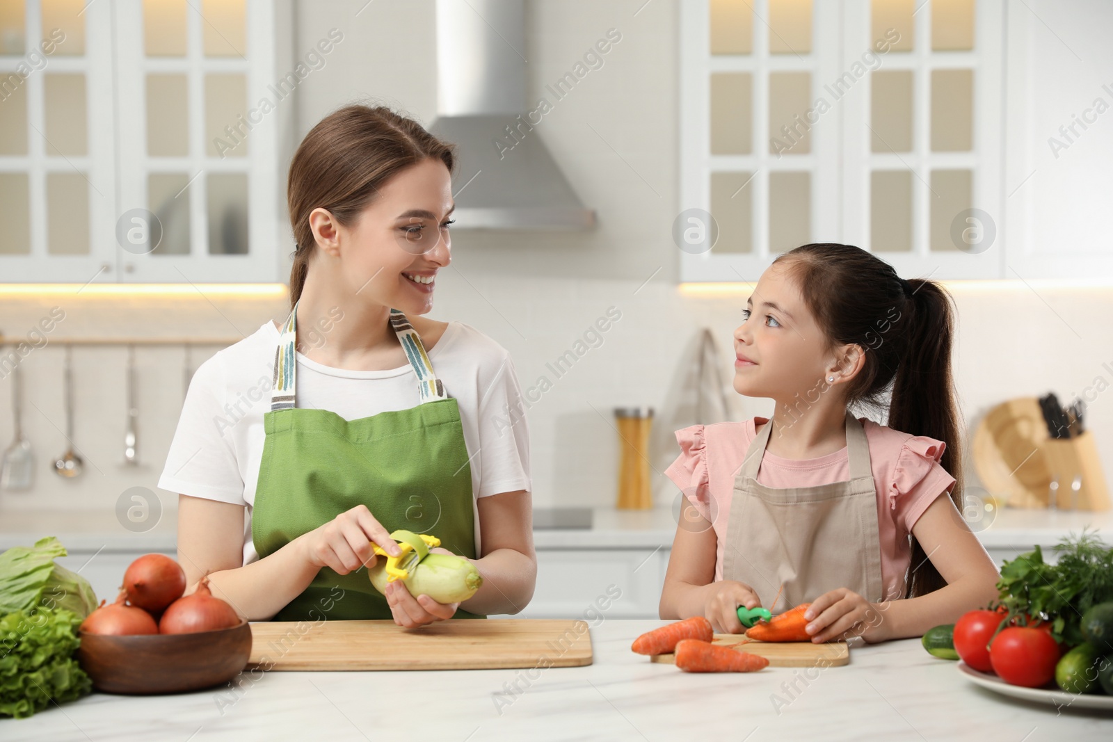 Photo of Mother and daughter peeling vegetables at table in kitchen