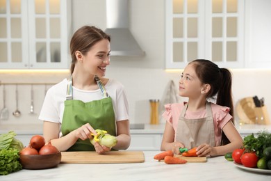 Mother and daughter peeling vegetables at table in kitchen