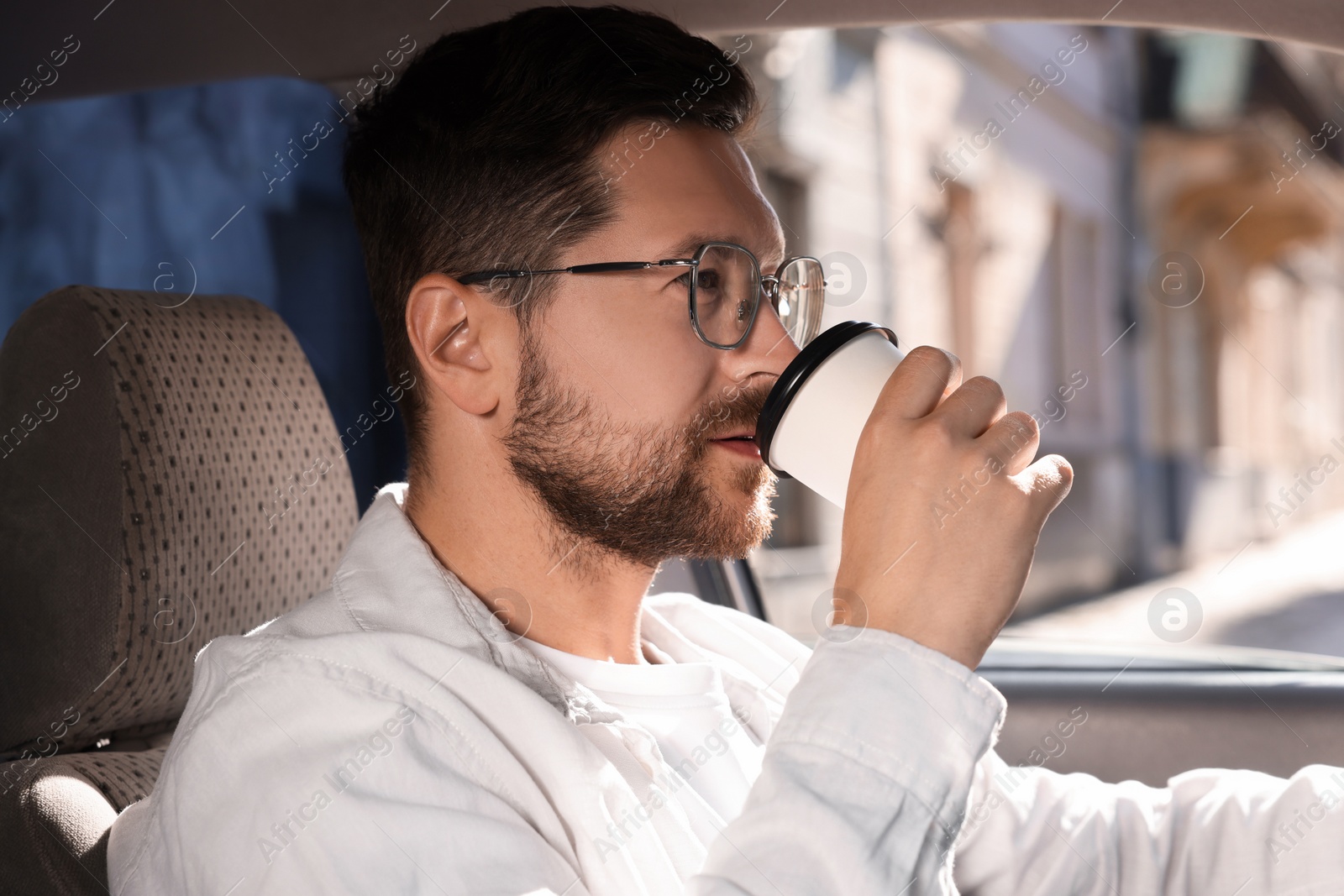 Photo of To-go drink. Handsome man drinking coffee in car