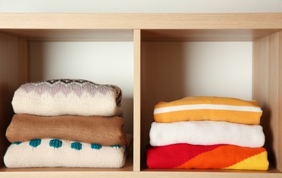 Photo of Stacks of folded winter clothes on shelves in wardrobe