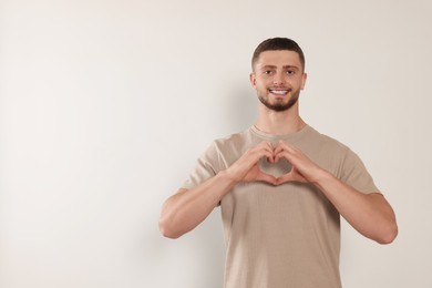 Photo of Happy volunteer making heart with his hands on light background. Space for text