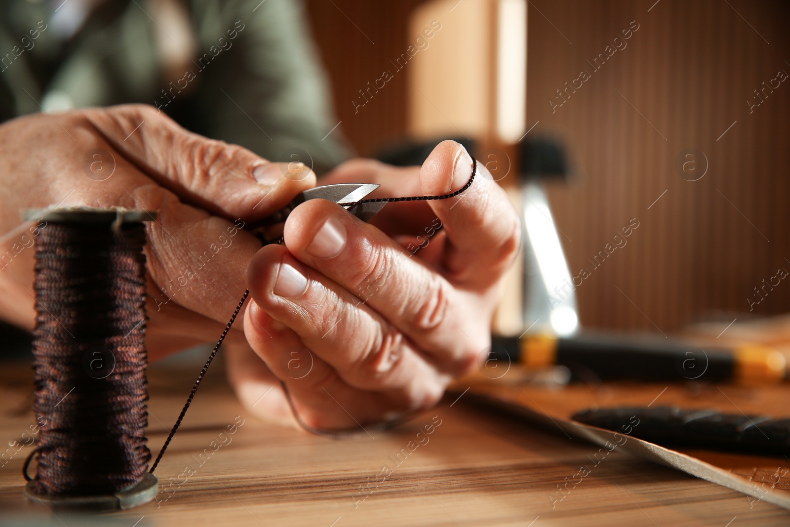 Photo of Man cutting thread while working with leather at table, closeup