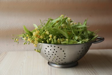 Photo of Beautiful linden blossoms and green leaves in metal colander on white wooden table