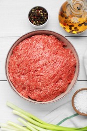 Bowl of raw fresh minced meat and ingredients on white wooden table, flat lay