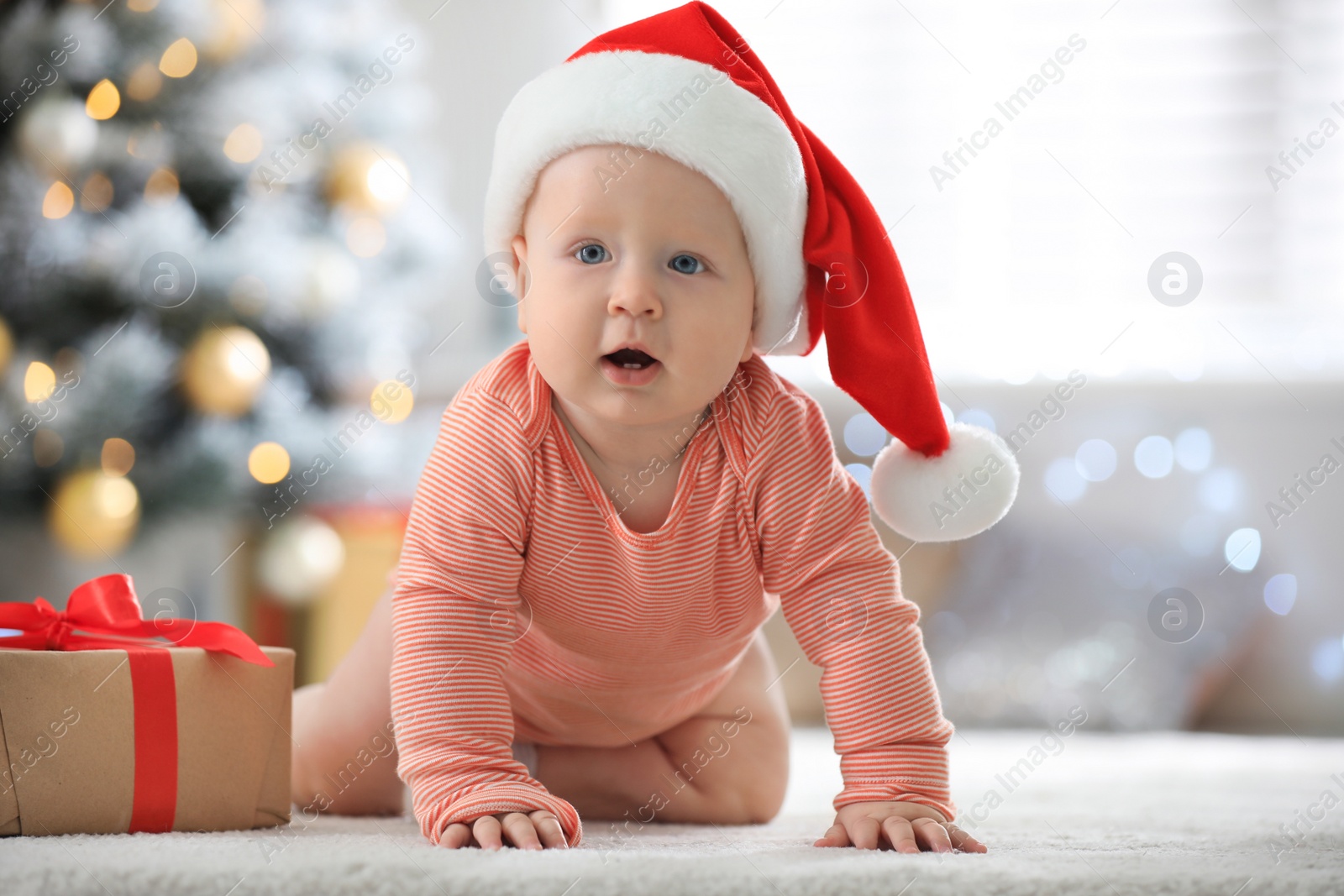 Photo of Little baby wearing Santa hat on floor indoors. First Christmas