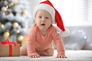 Photo of Little baby wearing Santa hat on floor indoors. First Christmas