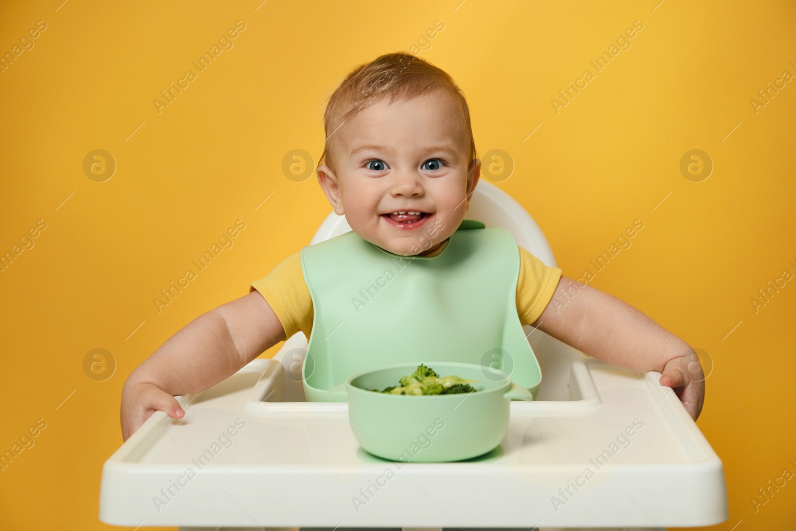 Photo of Cute little baby wearing bib while eating on yellow background