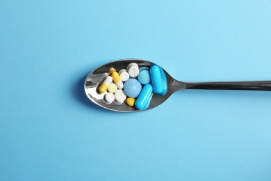 Spoon full of pills on color background, top view