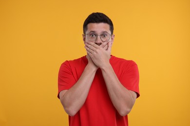 Photo of Embarrassed man covering mouth on orange background
