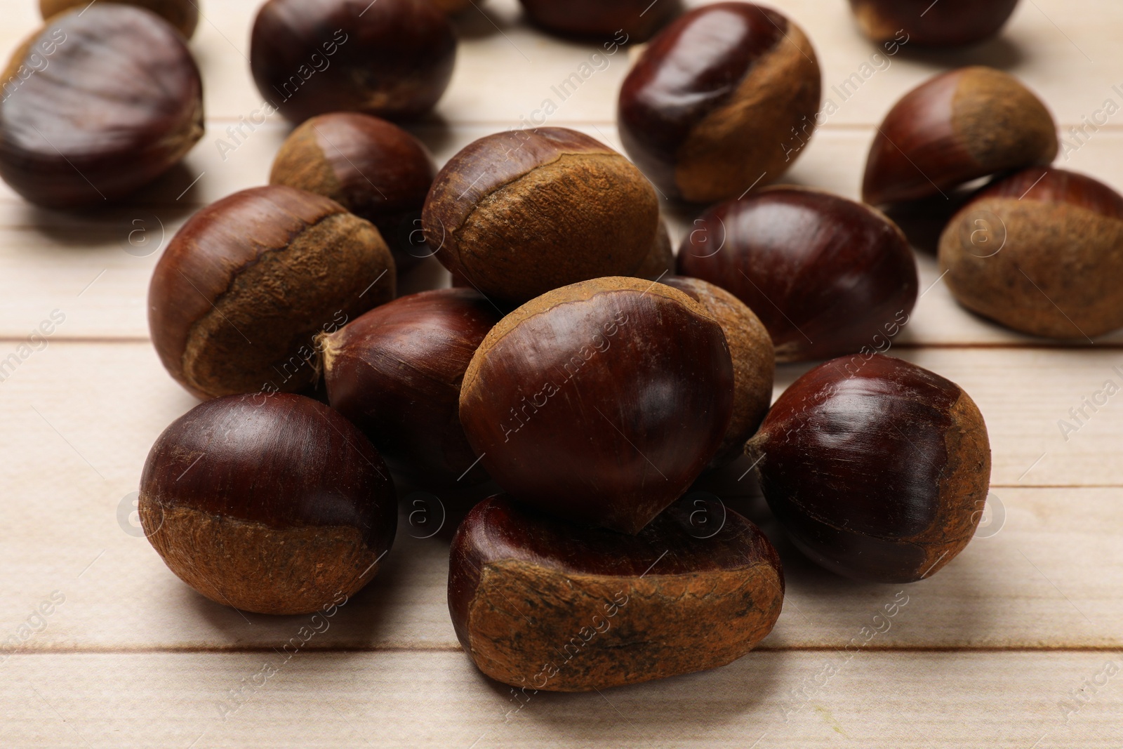 Photo of Sweet fresh edible chestnuts on light wooden table, closeup