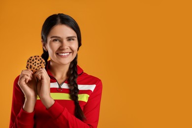 Young woman with chocolate chip cookie on orange background, space for text