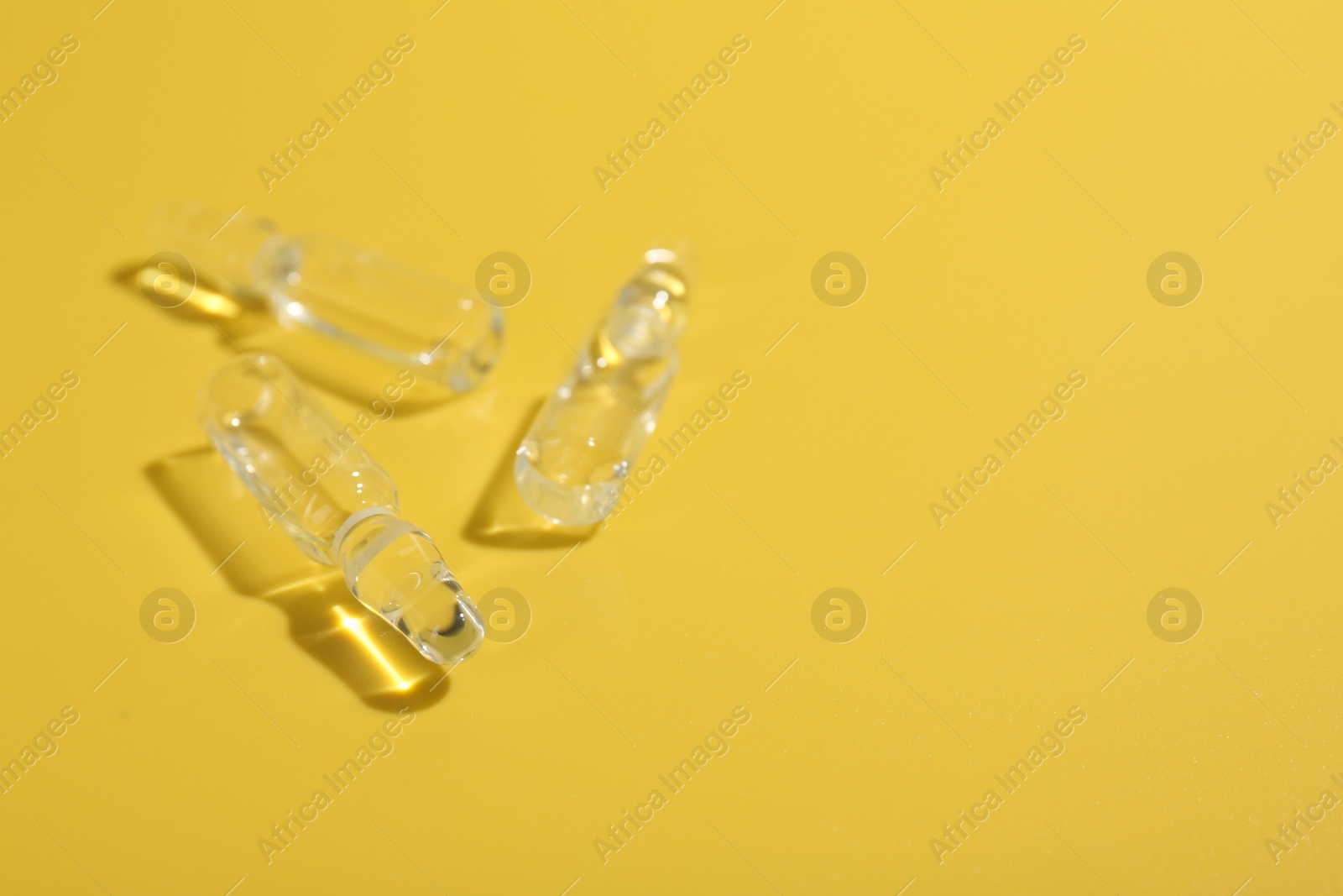 Photo of Glass ampoules with liquid on yellow background. Space for text