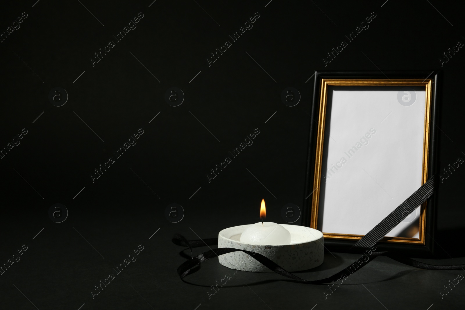 Photo of Funeral photo frame with ribbon and candle on black background. Space for design