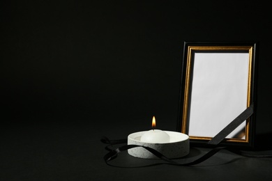 Photo of Funeral photo frame with ribbon and candle on black background. Space for design