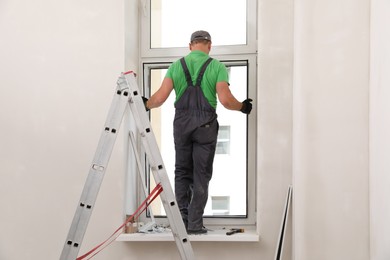 Photo of Worker in uniform installing double glazing window indoors, back view