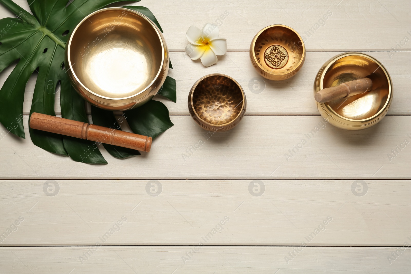 Photo of Flat lay composition with golden singing bowls on white wooden table. Space for text