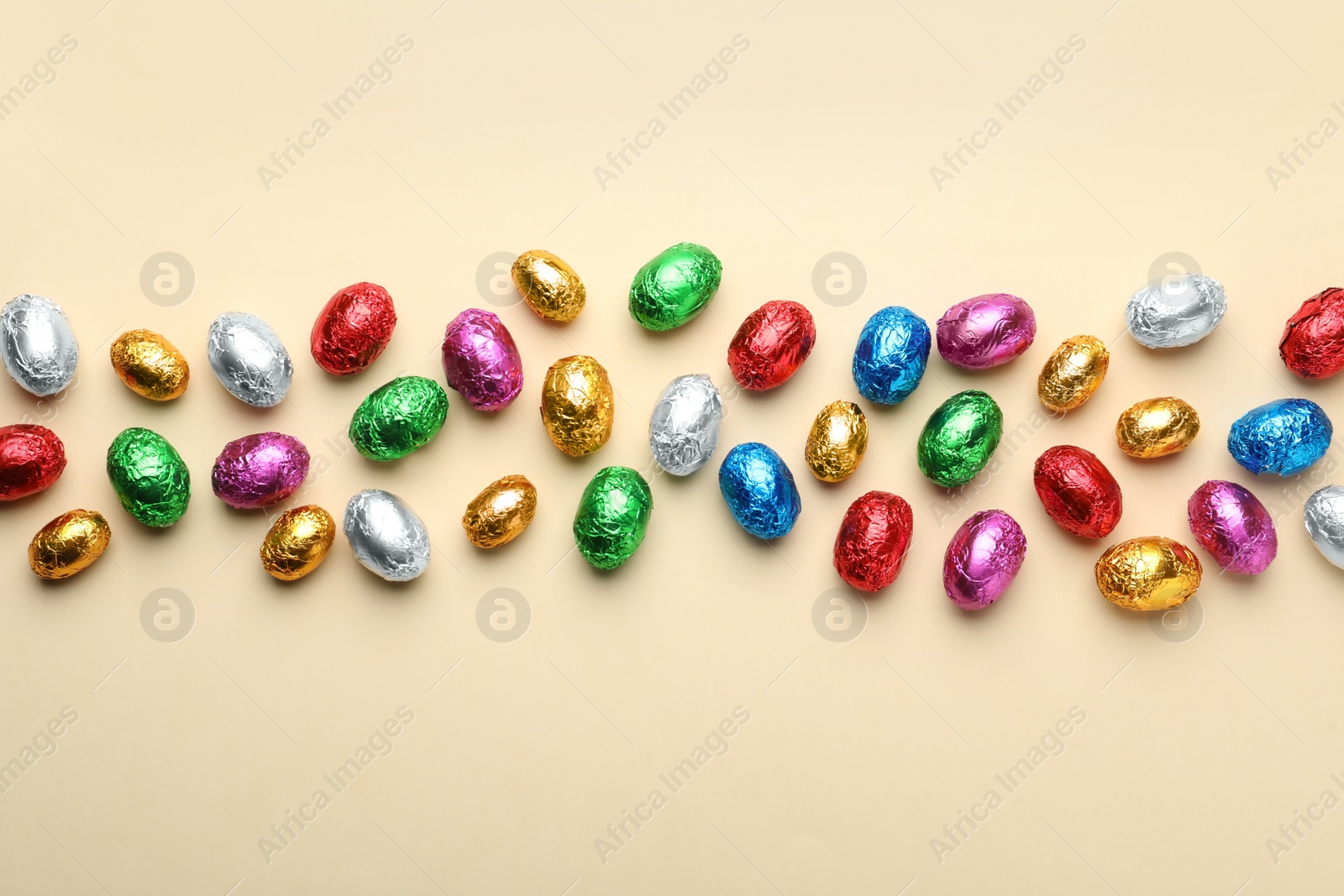 Photo of Chocolate eggs wrapped in colorful foil on beige background, flat lay