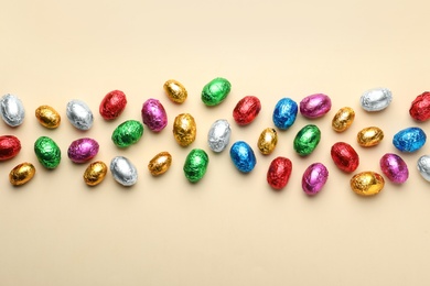 Chocolate eggs wrapped in colorful foil on beige background, flat lay