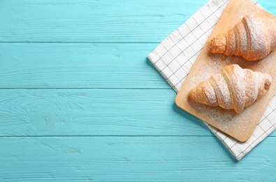 Photo of Wooden board with tasty croissants and space for text on light blue background, top view. French pastry