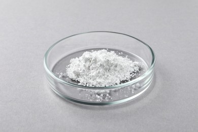 Photo of Petri dish with calcium carbonate powder on light grey table, closeup