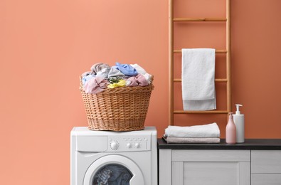 Photo of Wicker basket with dirty laundry on washing machine near coral wall indoors