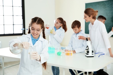 Schoolgirl making experiment with teacher and pupils in chemistry class