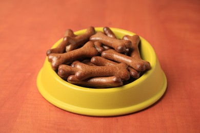 Yellow bowl with bone shaped dog cookies on wooden table, closeup