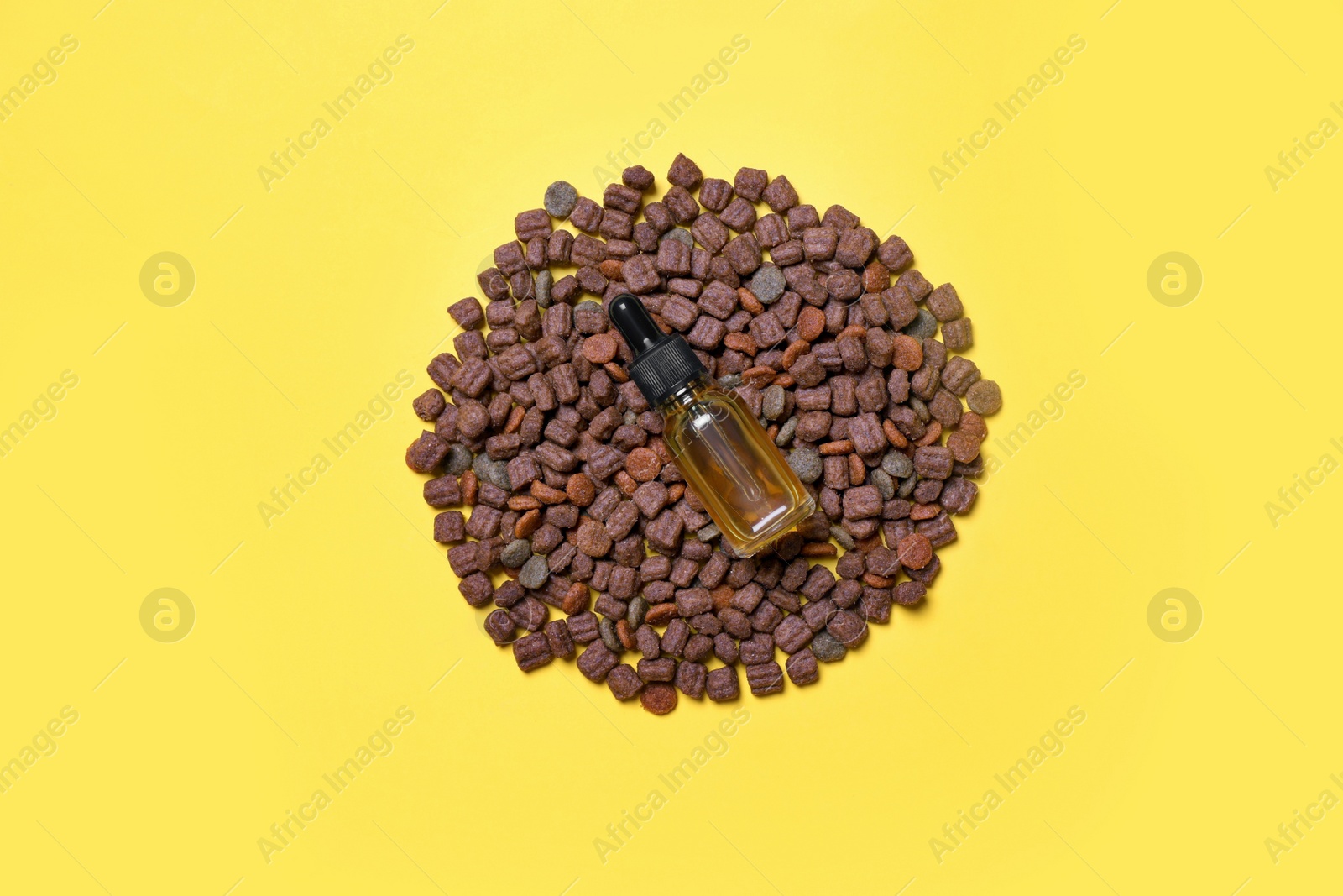 Photo of Glass bottle of tincture and dry pet food on yellow background, top view