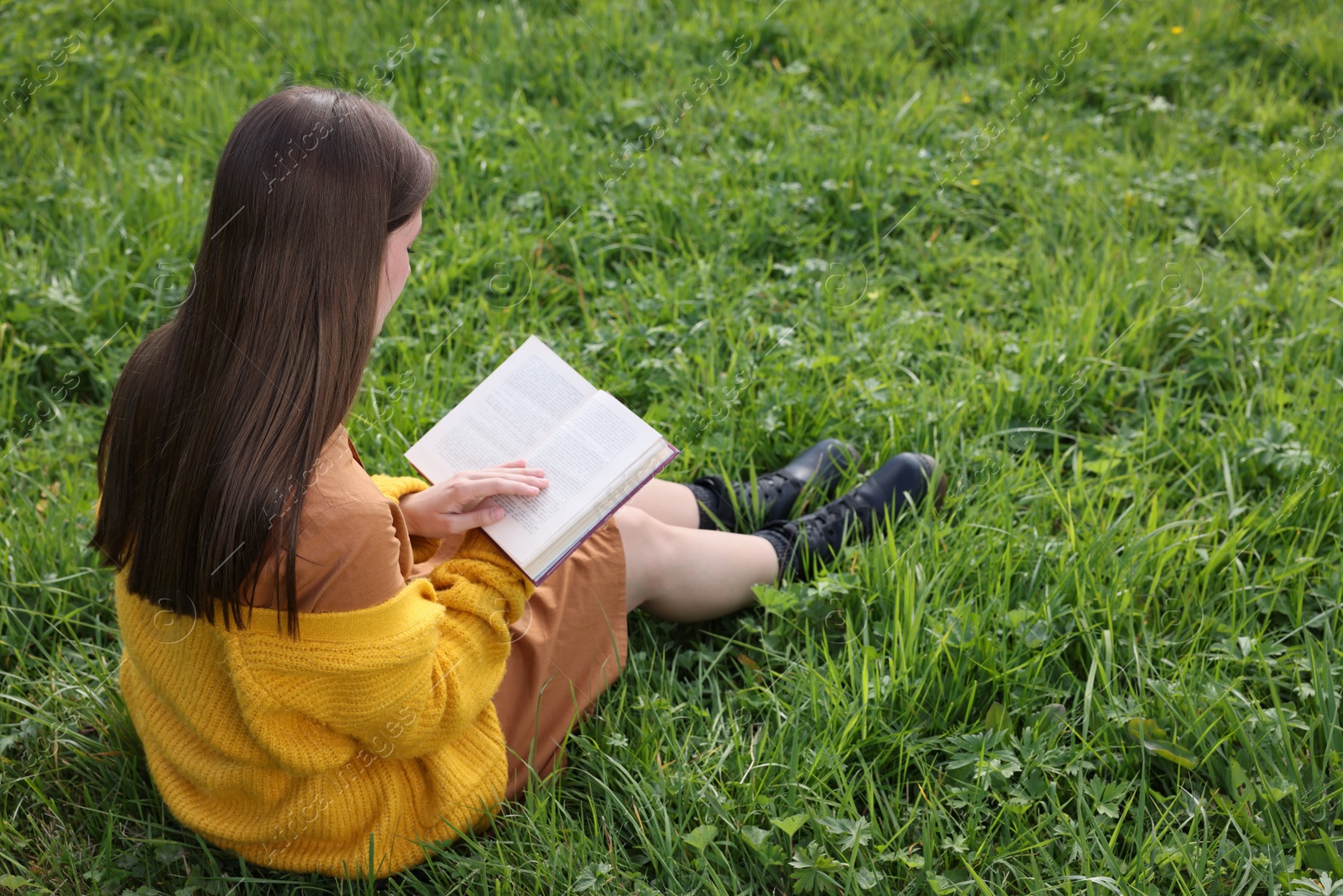 Photo of Young woman reading book on green grass