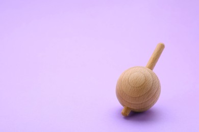 Photo of One wooden spinning top on lilac background, space for text. Toy whirligig