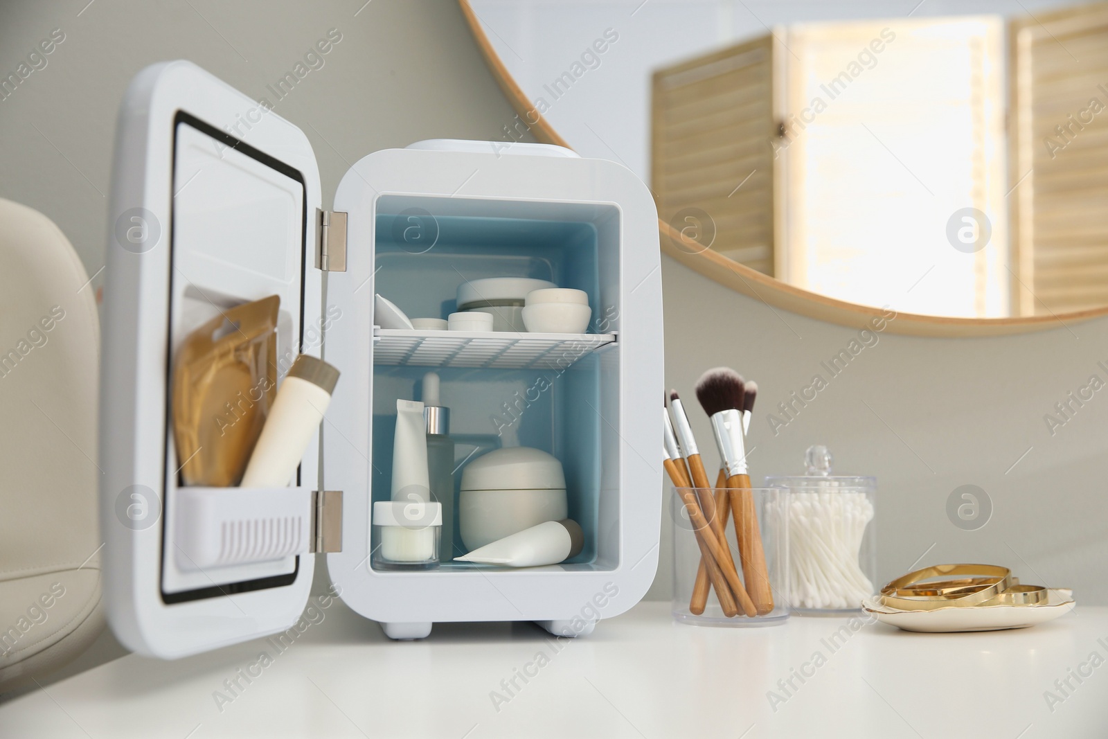 Photo of Cosmetics refrigerator and skin care products on white vanity table indoors