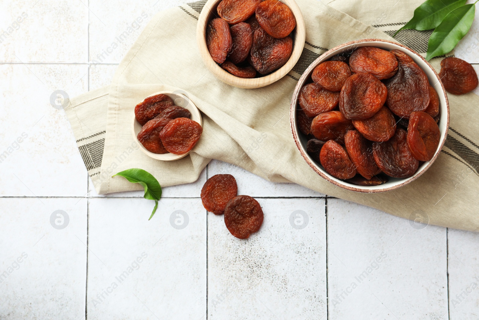 Photo of Tasty apricots, green leaves and space for text on white tiled table, flat lay. Dried fruits