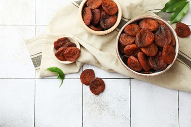 Photo of Tasty apricots, green leaves and space for text on white tiled table, flat lay. Dried fruits