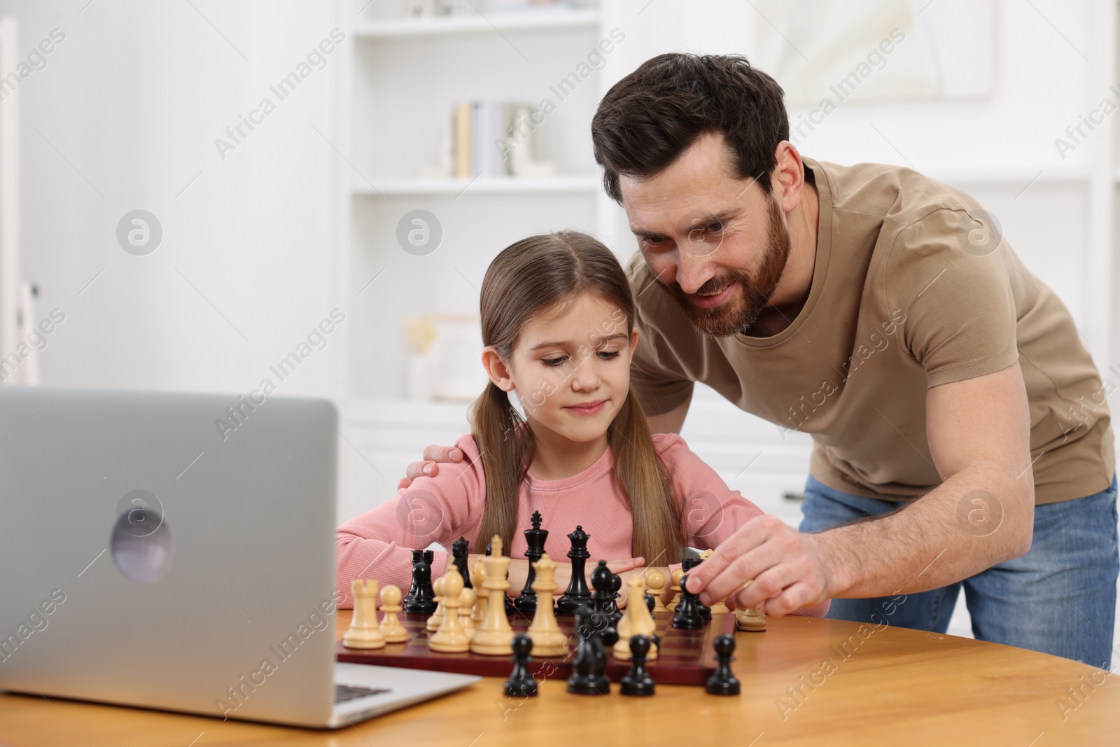 Photo of Father teaching his daughter to play chess following online lesson at home