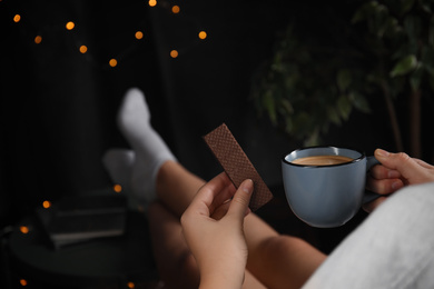 Woman with wafer and coffee on dark background, closeup. Early breakfast