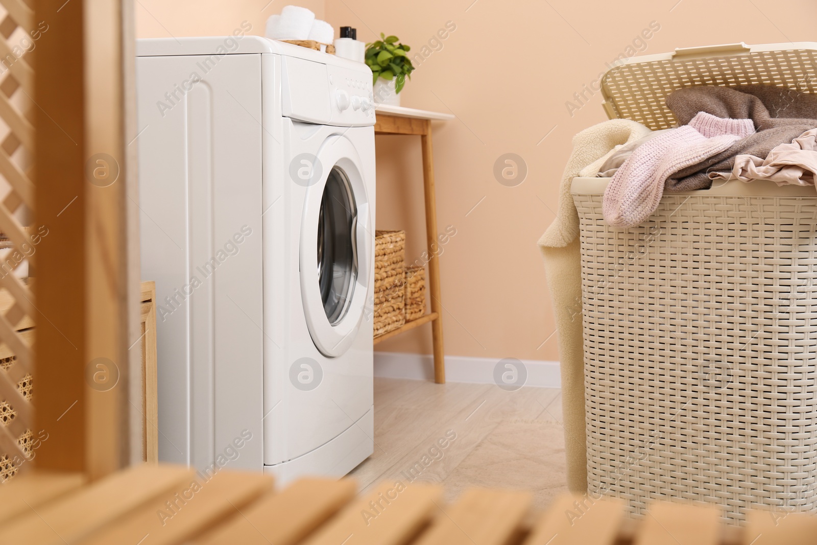 Photo of Laundry basket overfilled with clothes near washing machine in bathroom