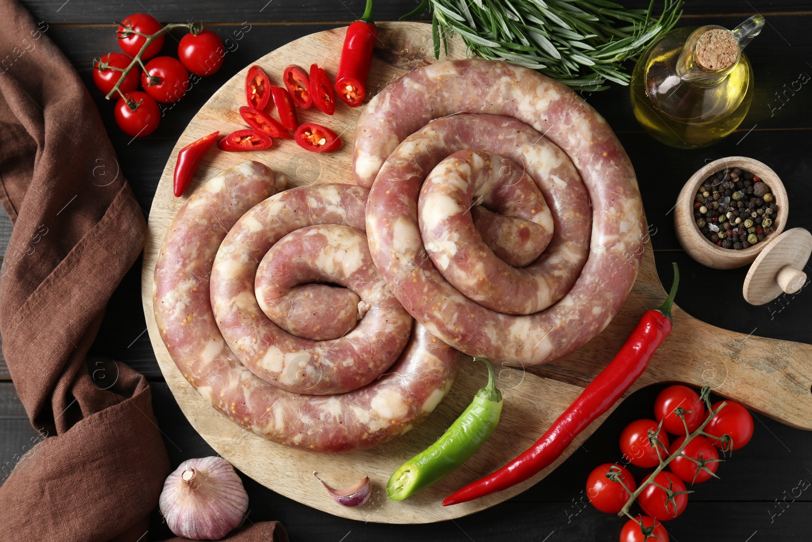 Photo of Raw homemade sausages, spices and other products on dark wooden table, flat lay