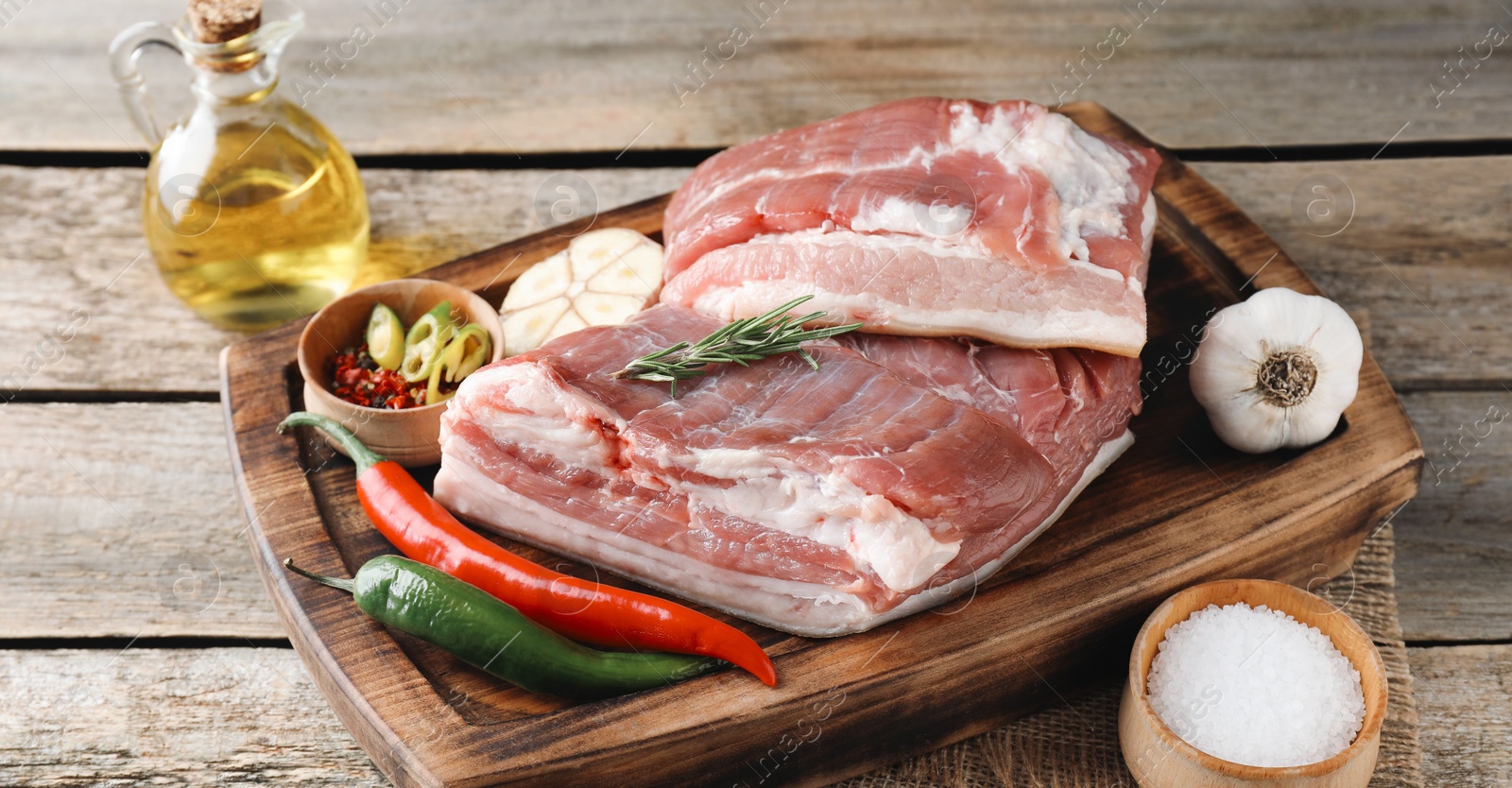 Photo of Pieces of raw pork belly, chili peppers, oil, garlic and rosemary on wooden table