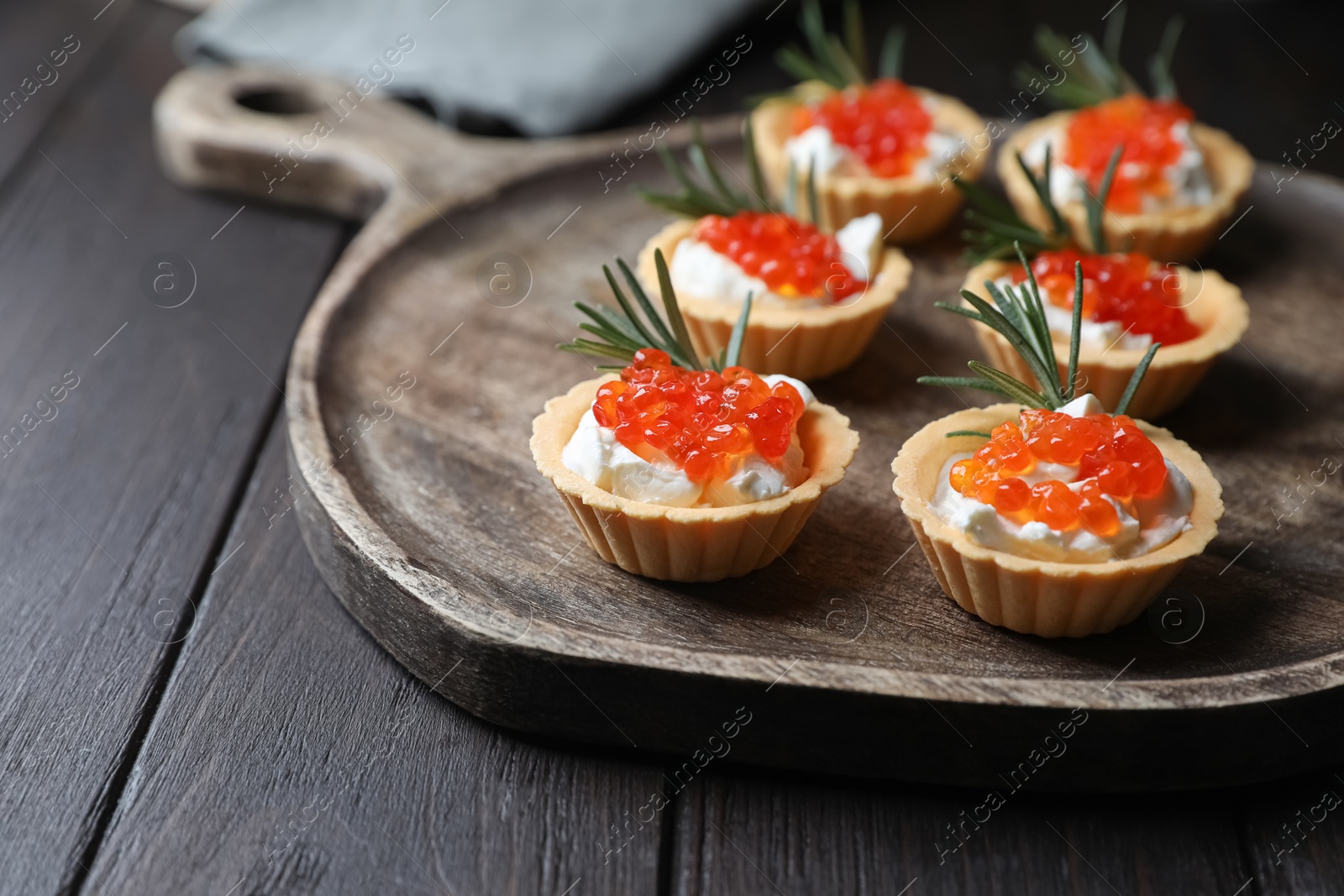 Photo of Delicious tartlets with red caviar and cream cheese served on wooden table, closeup. Space for text