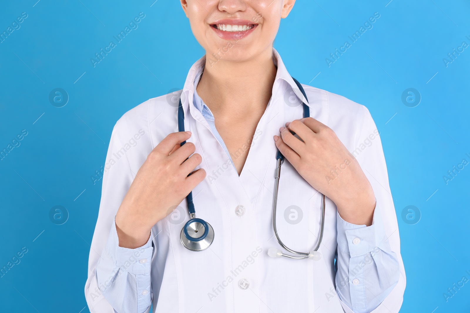 Photo of Young doctor with stethoscope on blue background, closeup